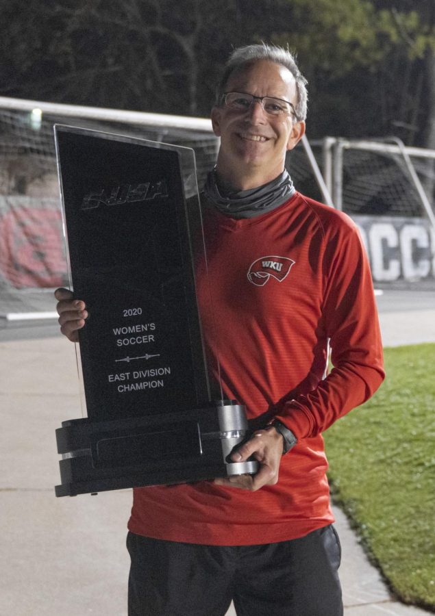 WKU soccer head coach Jason Neidell holding the first C-USA East Division title trophy in program history. Neidell has been the program's only coach in the team's existence. 